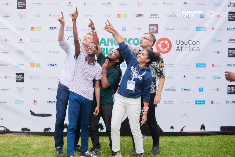 Five members of Djangonaut Space meeting up at DjangoCon Africa 2025, smiling and pointing to the sky!