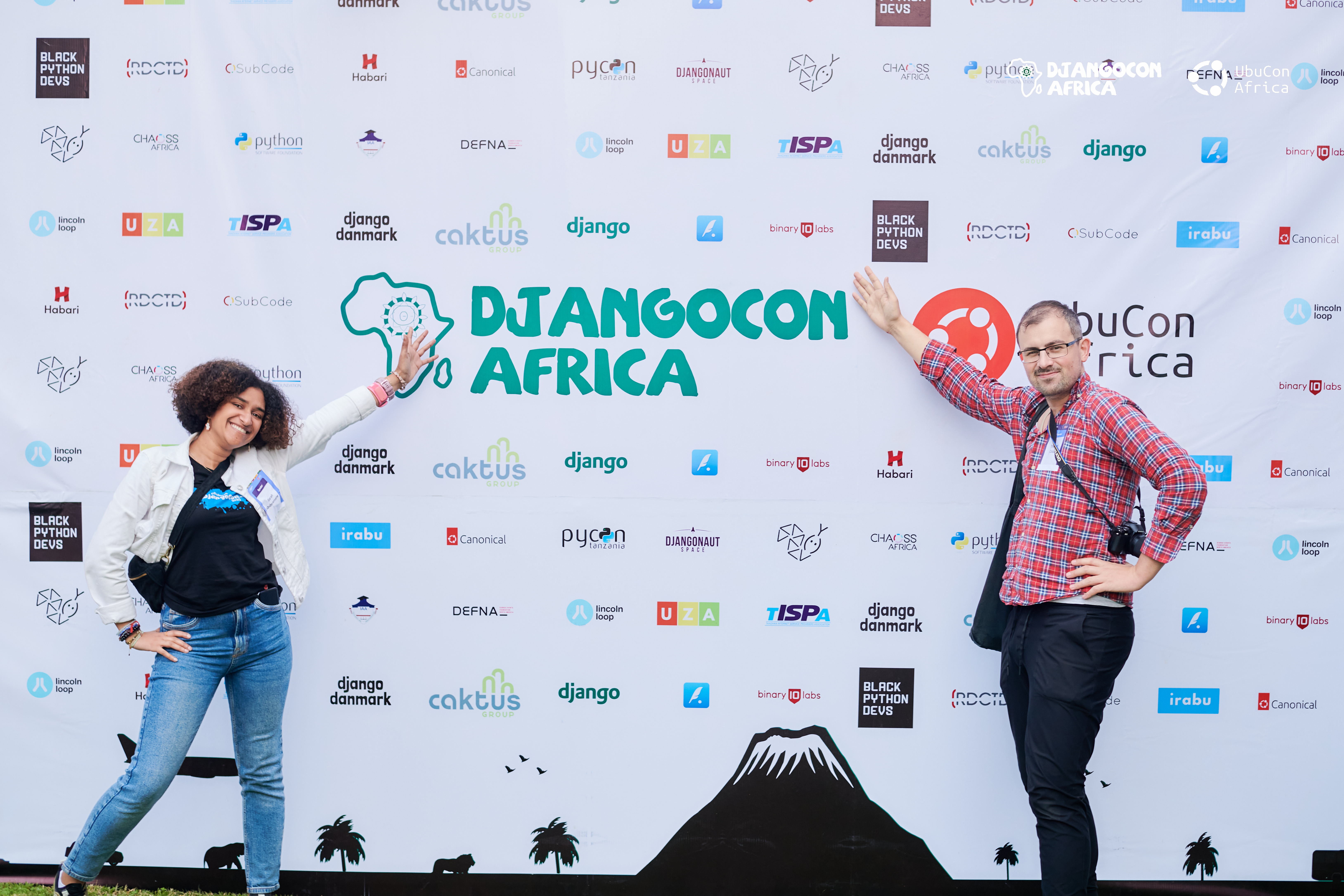 Thibaud Colas and I in front the wall of DjangoCon Africa UbuCon Africa with all sponsors logos. We are showing the name of the conference and both smiling.